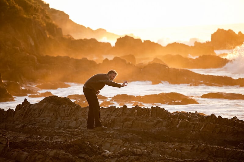 Figure of a man searching rocky wave platform bathed in golden dawn light