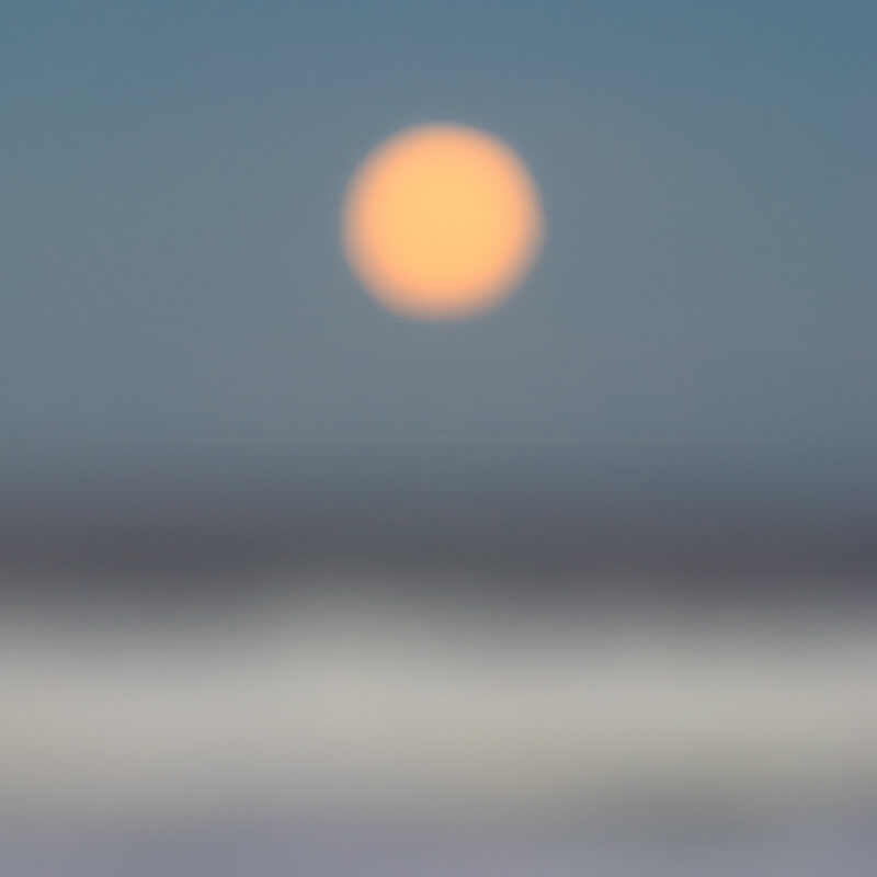 deliberately blurred square image of a full moon rising over the ocean