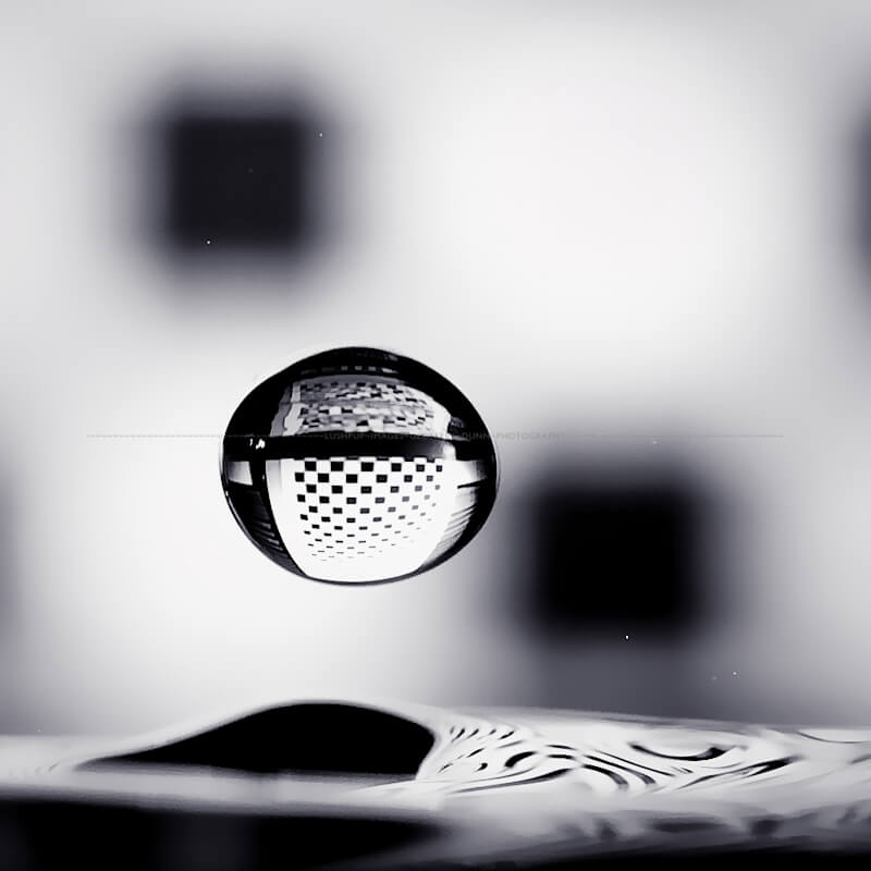 black and white image of a droplet falling and refracting a checkerboard background